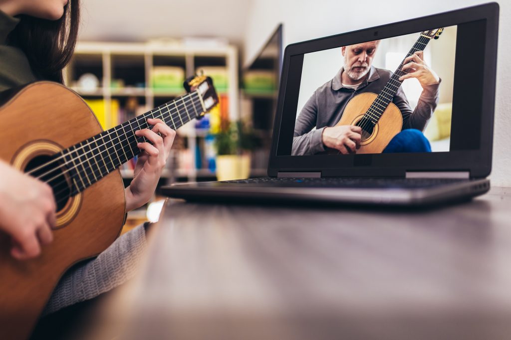 Focused girl playing acoustic guitar and watching online course